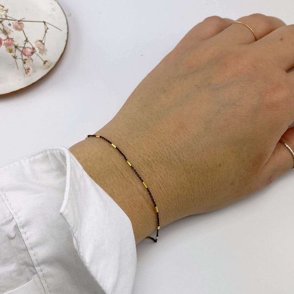 Close-up of wrist wearing delicate black chain bracelet, with gold rectangular bead accents.