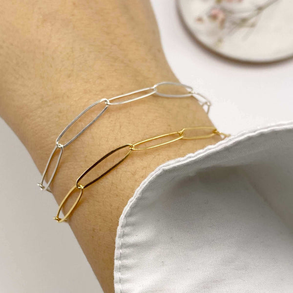 Close-up of hand wearing a gold and a silver bracelet of elongated links.