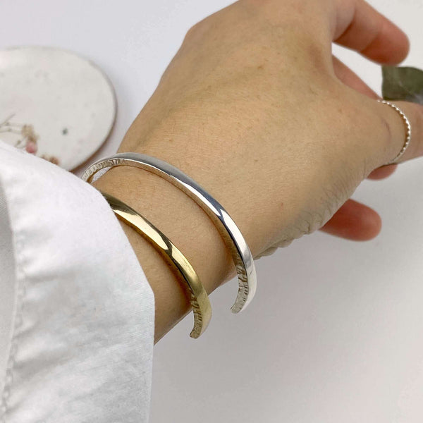 Close-up of wrist wearing a brass and a silver hand-hammered open cuff bracelet.