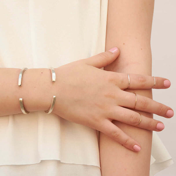 Close-up of arm wearing a brass and a silver hand-hammered open cuff bracelet, showing the open side.