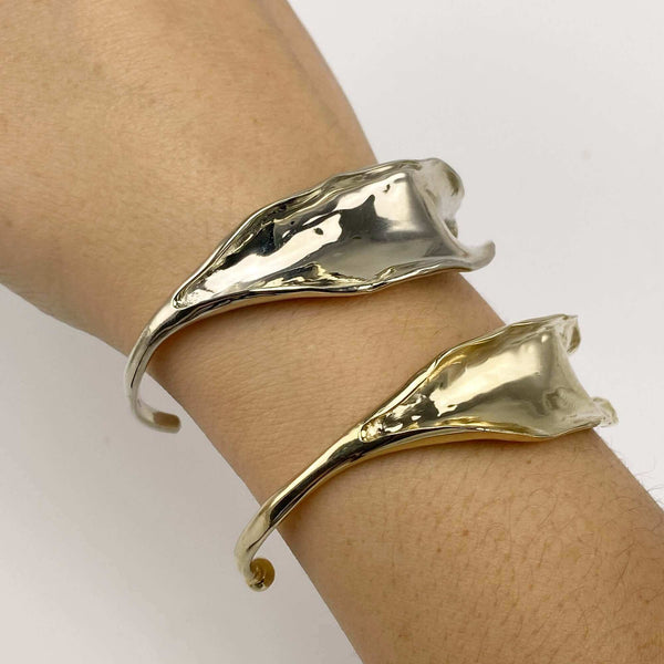 Close-up of hand wearing a polished white bronze and a polished brass open cuff bracelet with organic leaf motif.