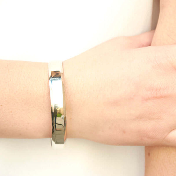Close-up of hand wearing heavy cuff bracelet with chamfered edges and overlapping ends, in polished white bronze.