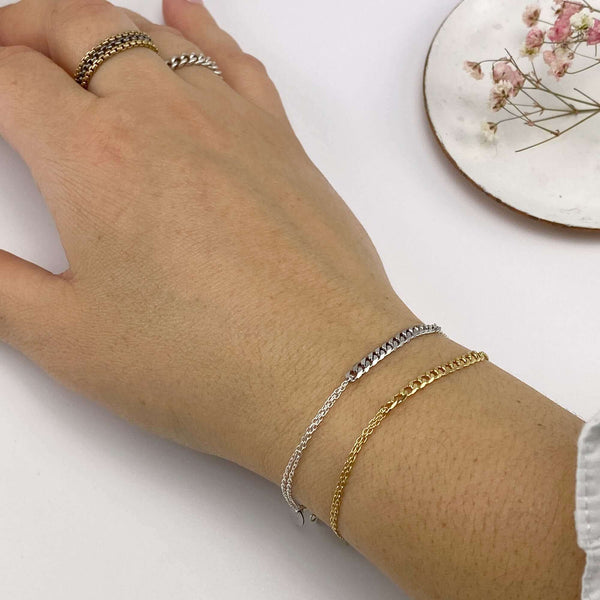 Close-up of hand wearing a gold and a silver delicate chain bracelet with curb chain detail at center.