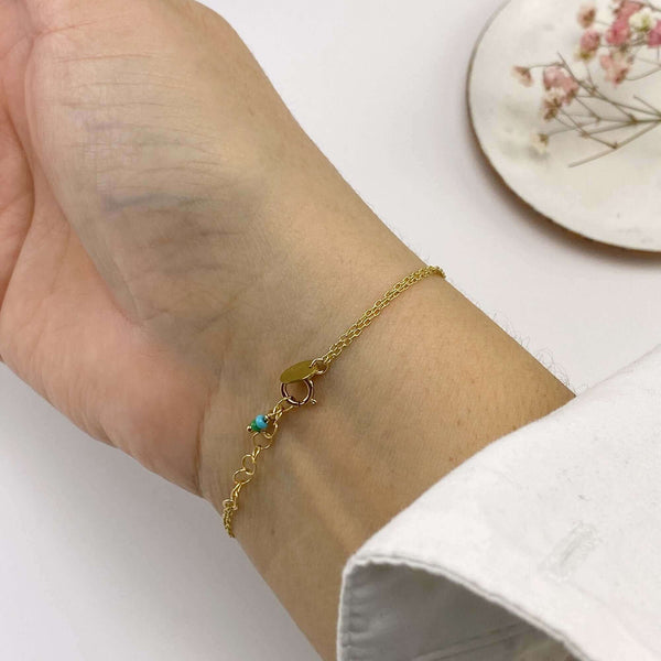 Close-up of hand wearing delicate gold chain bracelet showing tiny blue beads at clasp.