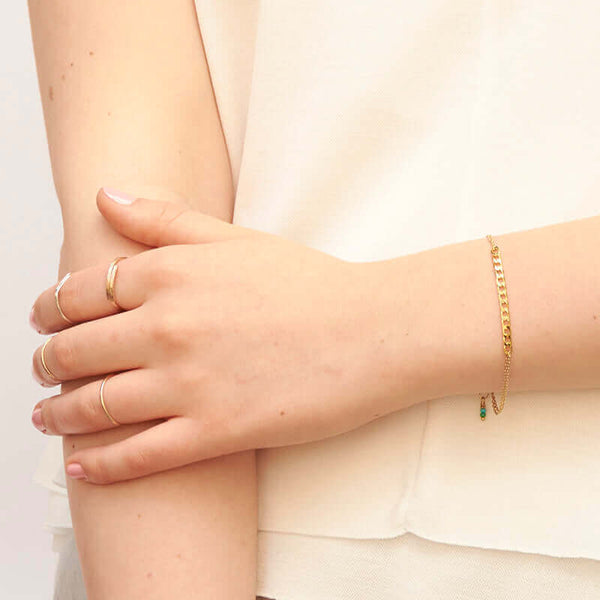 Close-up of arm wearing a gold and a silver delicate chain bracelet with curb chain detail at center.