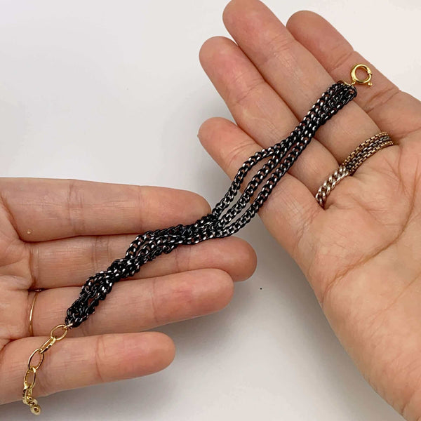 Close-up of hands holding bracelet with 3 twisted black oxidized chain showing gold links and clasp.