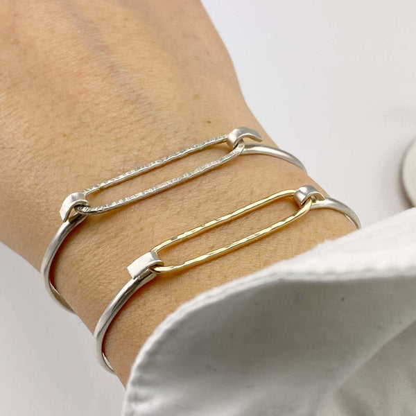 Close-up of hand wearing 2 simple bangle bracelets one with gold and one with silver hammered oval on silver cuff.