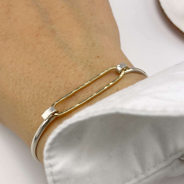 Close-up of hand wearing simple bangle bracelets with gold hammered oval on silver cuff.
