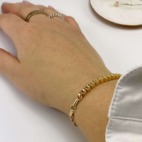 Close-up of hand wearing a chunky gold box chain bracelet.