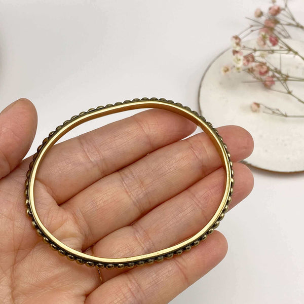 Close-up of fingers holding a polished brass beaded bangle bracelet.