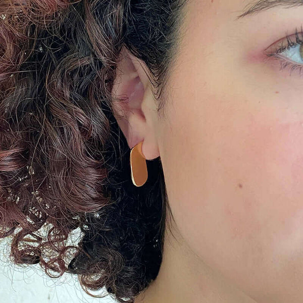 Close-up front view of woman wearing small flat oval earrings.