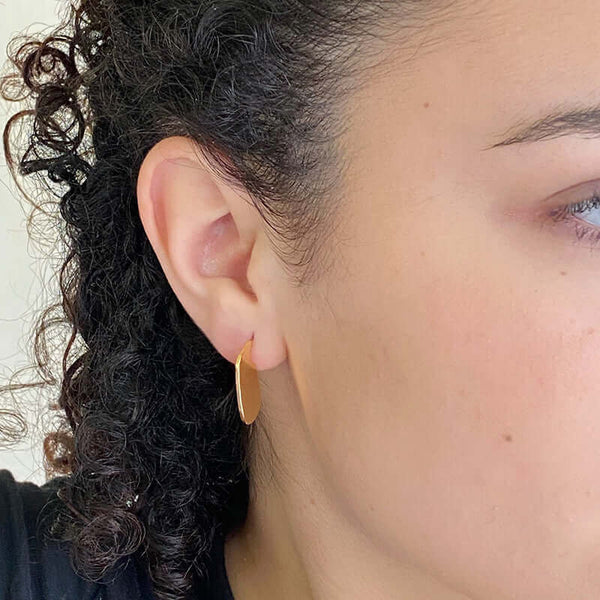 Close-up side view of woman wearing small flat oval earrings.