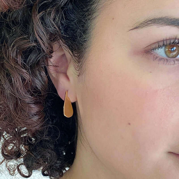Close-up front view of woman wearing small flat teardrop earrings.