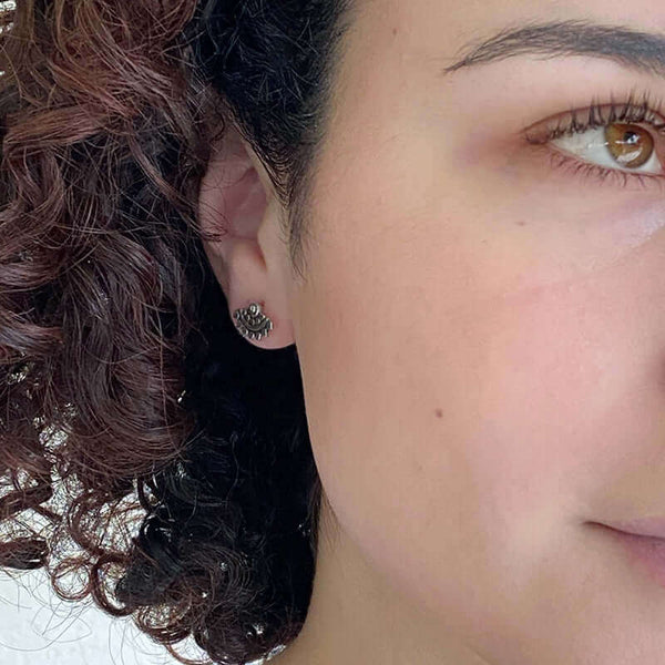 Close-up front view of woman wearing fan-shaped gold earrings with lace pattern, inset with small diamond.