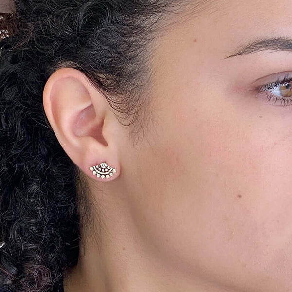 Close-up side view of woman wearing fan-shaped gold earrings with lace pattern, inset with small diamond.