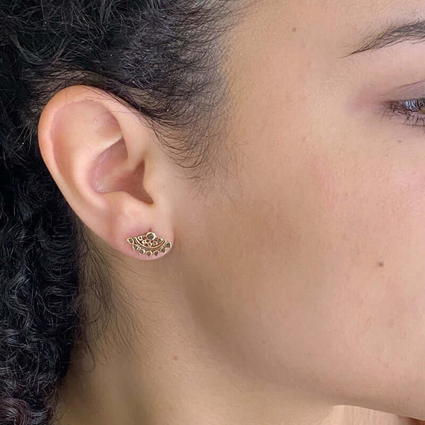Close-up side view of woman wearing fan-shaped gold earrings with lace pattern.