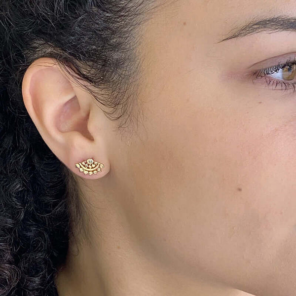 Close-up side view of woman wearing fan-shaped gold earrings with lace pattern, inset with small sapphire.