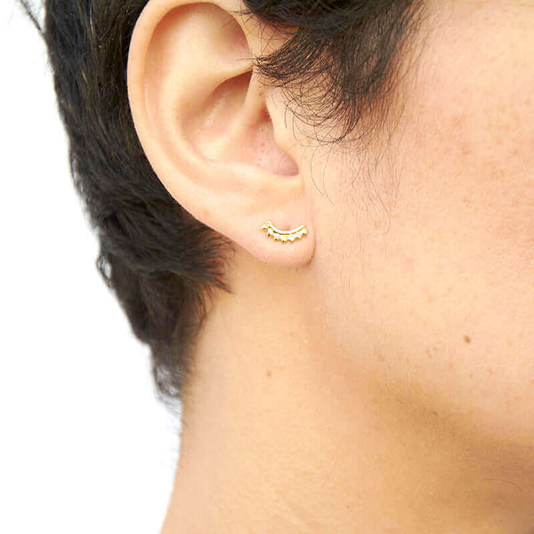 Close-up side view of woman wearing gold earrings, arc-shaped with little triangular beads.