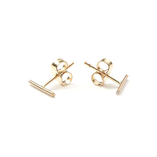 Pair of gold bar earrings on earpost facing out.