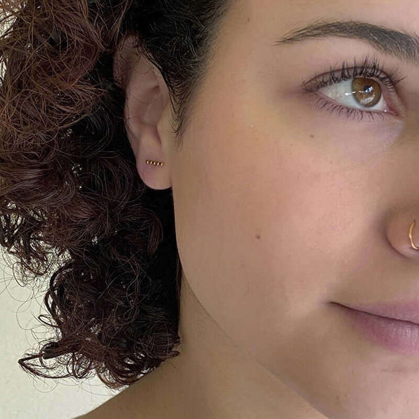 Close-up front view of woman wearing gold beaded bar earrings on earpost.