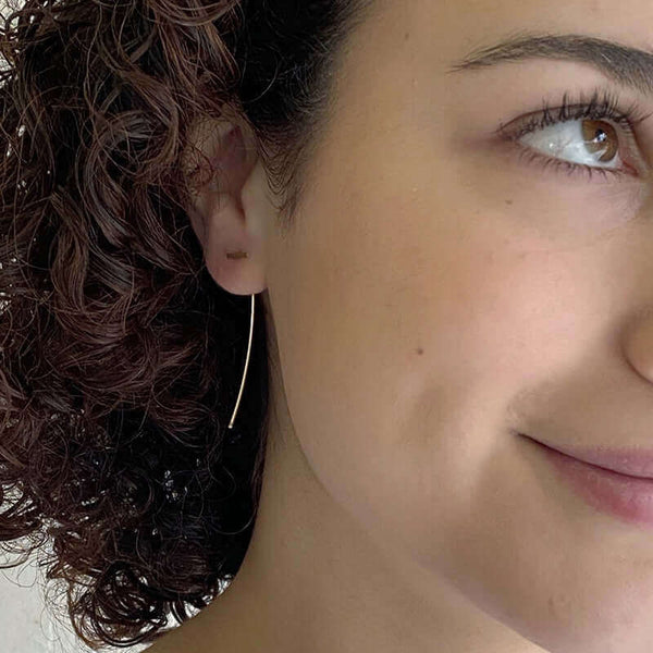 Close-up front view of woman wearing gold bar threader earrings with wire bar extending down.