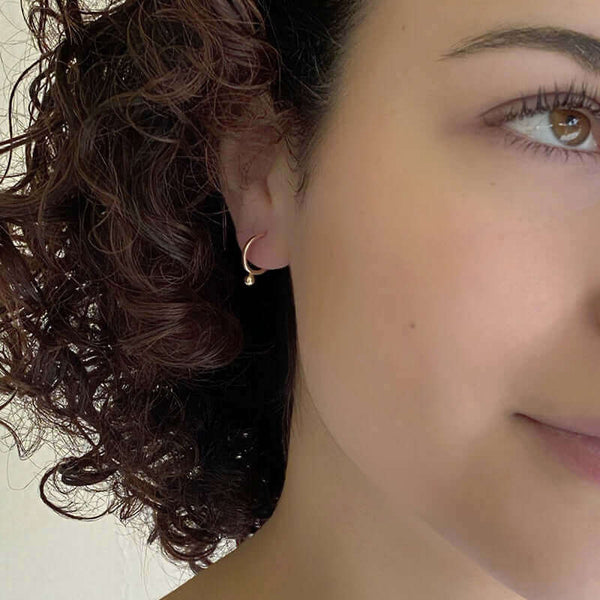 Close-up front view of woman wearing small gold hoop earring with small dot bead on bottom.