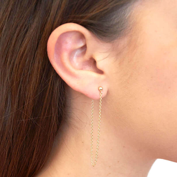 Side view of woman wearing gold earrings, long loop of delicate chain on a post.