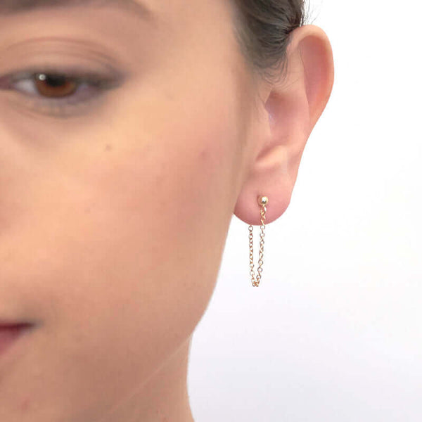 Front view of woman wearing gold earrings, short loop of delicate chain on a post.
