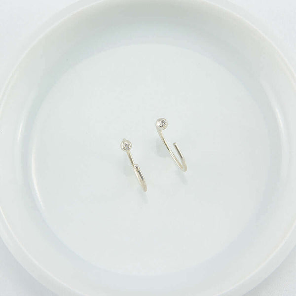 Pair of small silver hoop earring, tiny ball detail in front with inset diamond, facing up.
