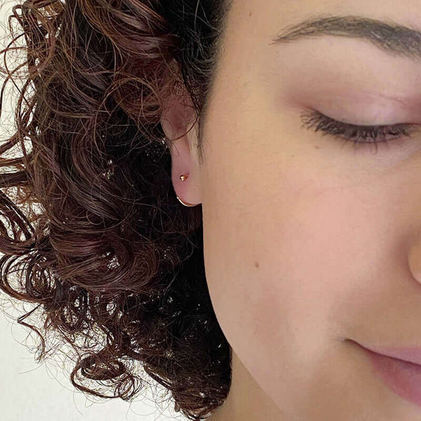 Close up front view of woman wearing small gold hoop earring with a tiny ball detail in front, facing in.
