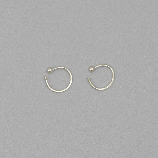 Pair of small silver hoop earring with a tiny ball detail in front, facing sideways.
