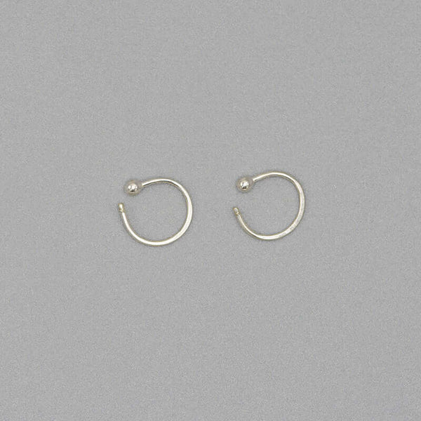 Pair of small silver hoop earring with a tiny ball detail in front, facing sideways.