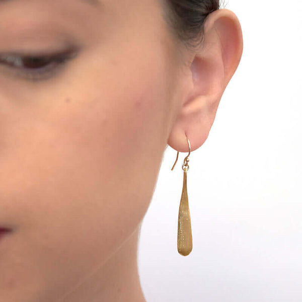 Close up front view of woman wearing gold earrings shaped like elongated teardrop.