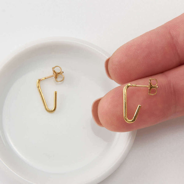 Finger holding one of a pair of gold bent angle earrings on posts