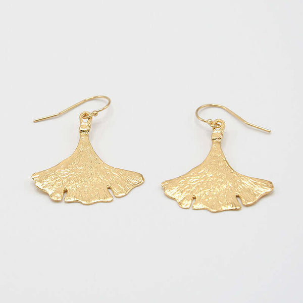 Pair of gold earrings shaped like ginko leaves, shown at low angle.