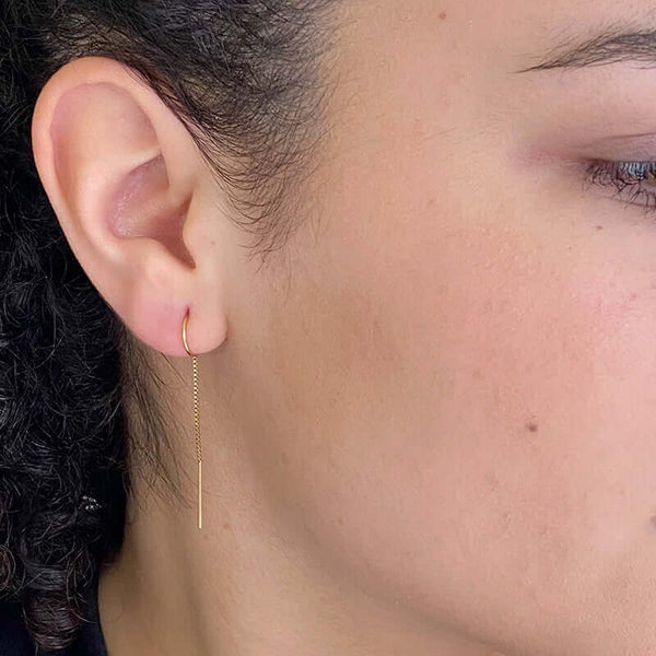 Close-up side view of woman wearing gold earrings, with open hoop with thin chain hanging down.