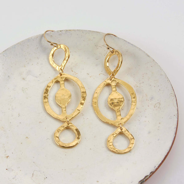 A Pair of Itza Hammered Dangle Earrings Displayed on a Marble Plate