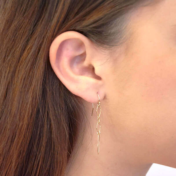 Close up side view of woman wearing gold oval chain earrings, with large oval link at end.