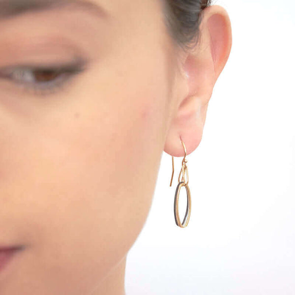 Close up front view of woman wearing pair of earrings with silver, black and gold colored oval links on gold earwire.