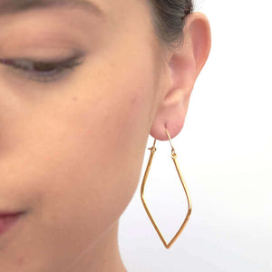 Close up front view of woman wearing pair of silver geometric rhombus shaped hoop earrings.