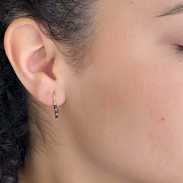 Close up side view of woman wearing pair of small gold wire earrings with black and gold beads.