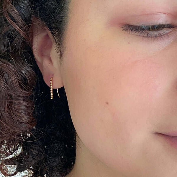 Close up front view of woman wearing pair of small gold wire earrings with gold beads.