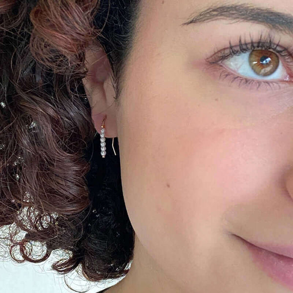 Close up front view of woman wearing pair of small gold wire earrings with pearl beads.