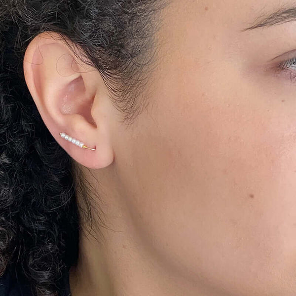 Close up side view of woman wearing pair of small gold wire earrings with pearl beads.