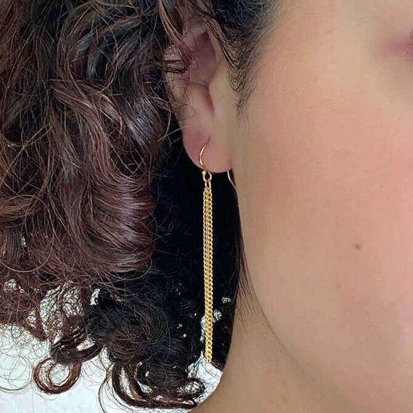 Close up front view of woman wearing pair of of gold chain tassel earrings, on earwire.