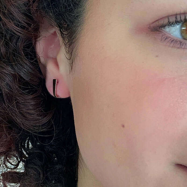 Close up side view of woman wearing pair of tiny gold post cuff earrings that wrap around earlobe.