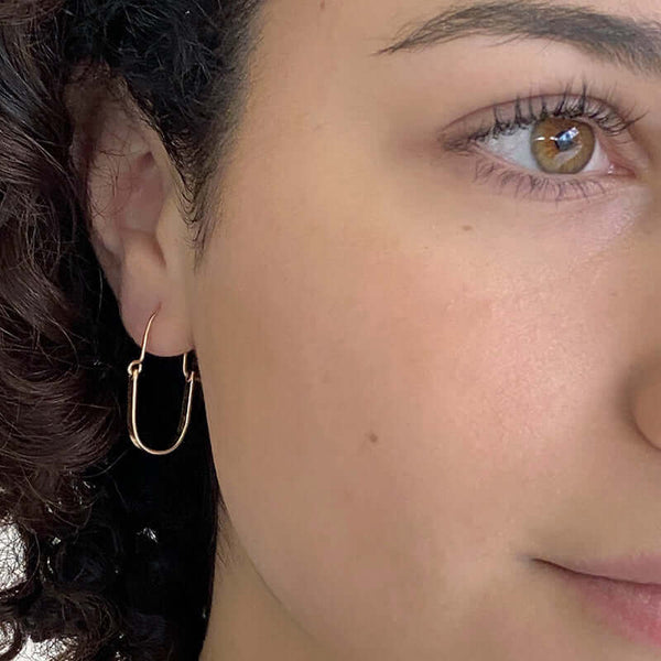 Close up front view of woman wearing pair of gold hoop style earrings with curved bar on wire.