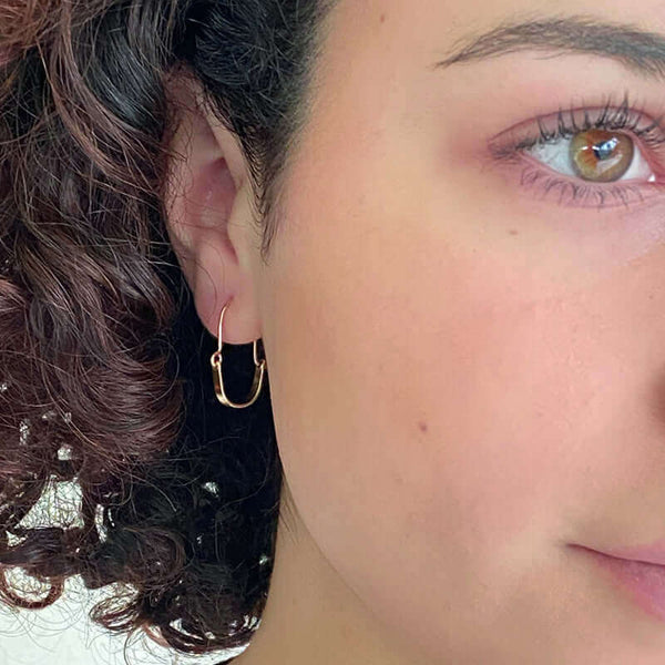 Close up front view of woman wearing pair of small gold hoop style earrings with curved bar on wire.