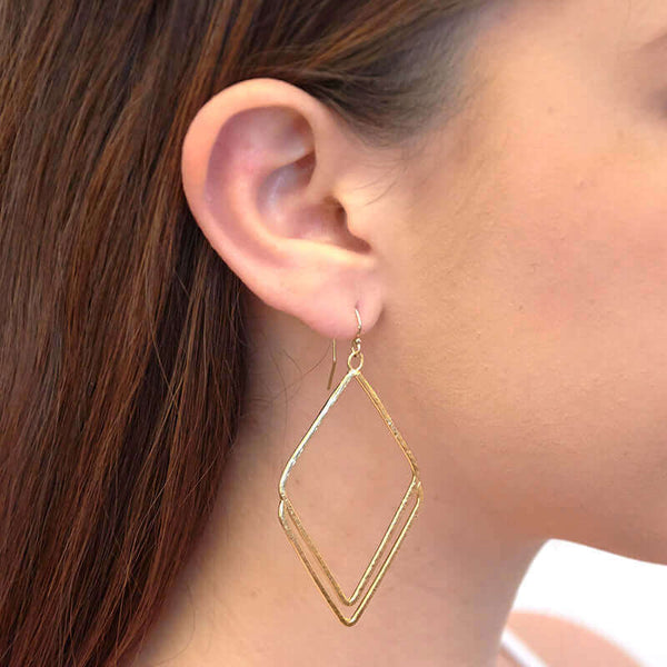 Close-up side view of woman wearing a pair of gold rhombus shaped earrings.