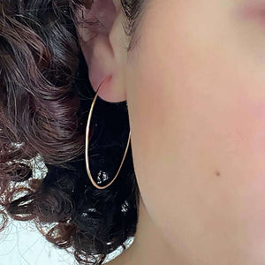 Close-up front view of woman wearing a pair of simple gold hoop earrings with loop and hook as clasp.